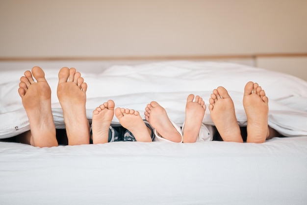 Dormir, relajarse y pies con la familia en el dormitorio para una mañana tranquila y amor. Cuidar, apoyar y despertar con un primer plano de padres e hijos en la cama en casa para disfrutar de la paz del fin de semana y descansar juntos.