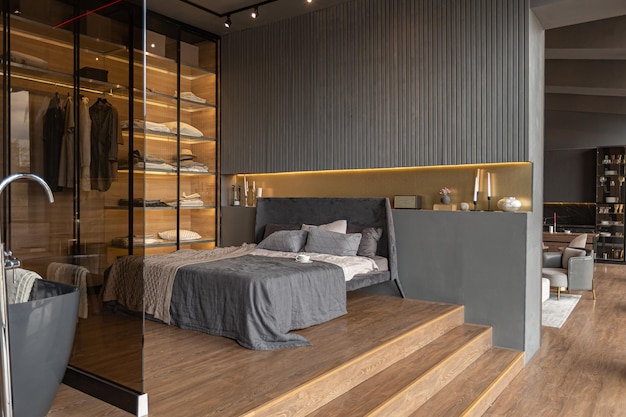 Dormitorio y baño independiente detrás de una partición de vidrio en un elegante y caro interior de una casa de lujo con un diseño oscuro y moderno con molduras de madera y luz LED
