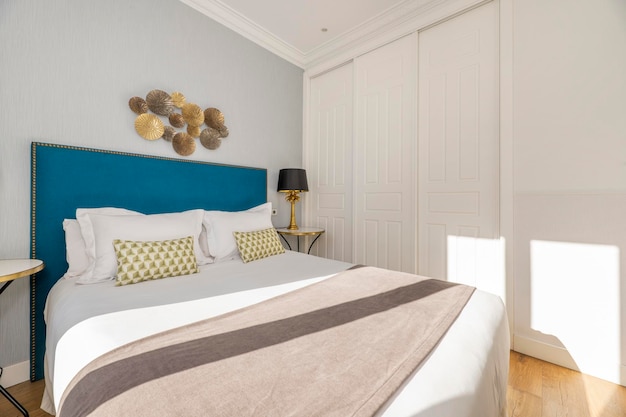 Dormitorio con cabecero de madera tapizado con cojines y almohadas de terciopelo azul y un precioso armario empotrado con puertas correderas blancas
