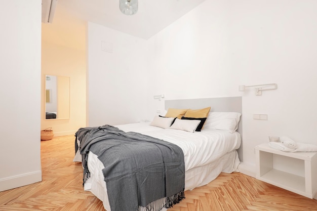 Foto dormitorio con cama grande con muchos cojines dos mesitas de noche con lámparas retráctiles carpintería blanca en puertas tocador con espejo y aire acondicionado y piso de pino barnizado