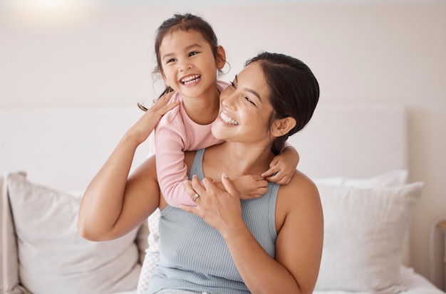 Foto dormitorio feliz y sonrisa de madre y niña descansando y pasando tiempo juntos en unas vacaciones relaja la felicidad y calma a la mujer y su hijo sentados en una cama y abrazándose en una habitación de su casa familiar