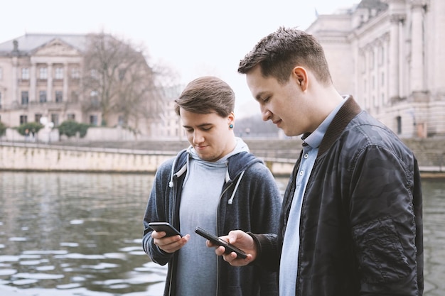 Dos adolescentes adictos a los teléfonos móviles de pie juntos mirando el teléfono inteligente