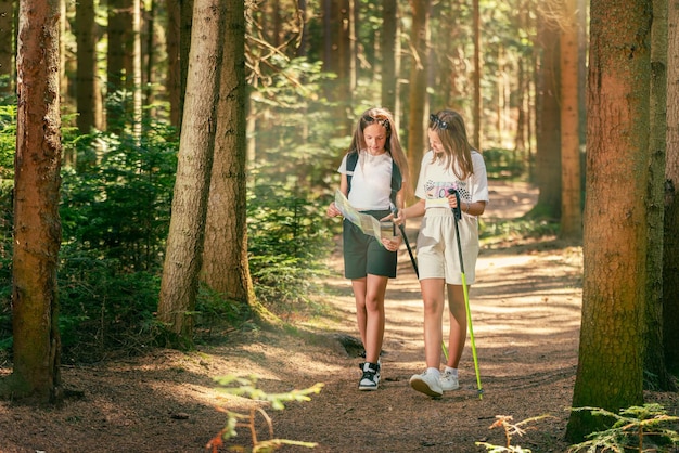 Dos adolescentes caminan por el bosque leyendo un mapa de papel con bastones de senderismo y mochilas