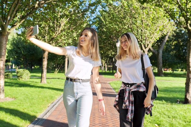 Dos adolescentes felices mirando la cámara web del teléfono inteligente, las niñas toman fotos selfie, hablan en línea con amigos. Estilo de vida juvenil, adolescentes, comunicación, amistad.