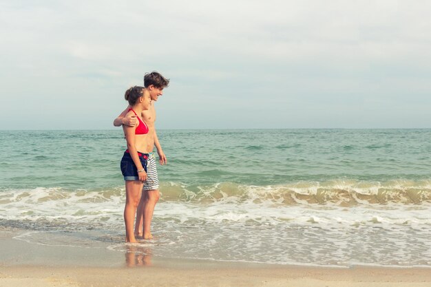 Dos adolescentes, una niña y un niño con cabello rubio vestidos con traje de baño, caminan en una playa de mar