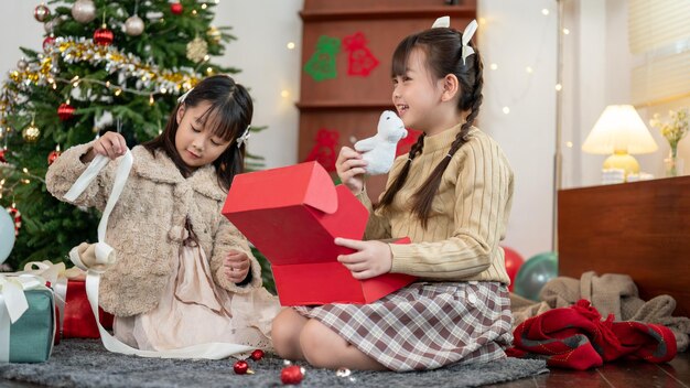 Dos adorables jóvenes asiáticas disfrutan juntas abriendo su regalo de Navidad en casa