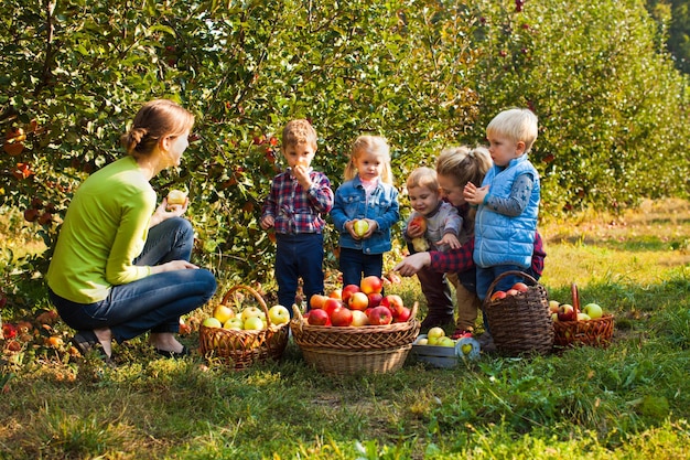 Dos adorables mujeres jóvenes entre manzanos llenos de frutos maduros en la eco-granja. Tutores con preescolares en excursión.