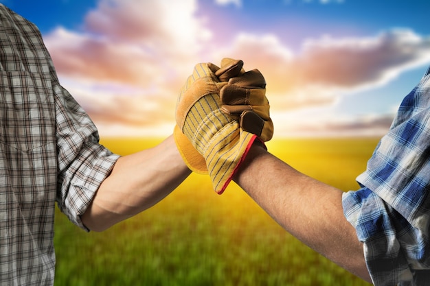 Dos agricultores masculinos en guantes un apretón de manos al atardecer