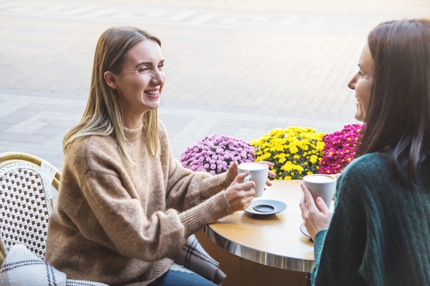 Dos alegres amigas beben capuchino en una cafetería de la calle de la ciudad.