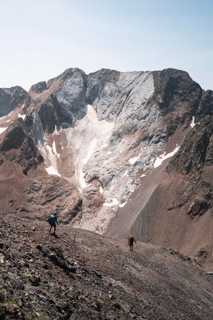 Foto dos alpinistas caminan a lo largo de la cresta con los picos de los infiernos en el fondo en el impresionante paisaje de las montañas de los pirineos en huesca