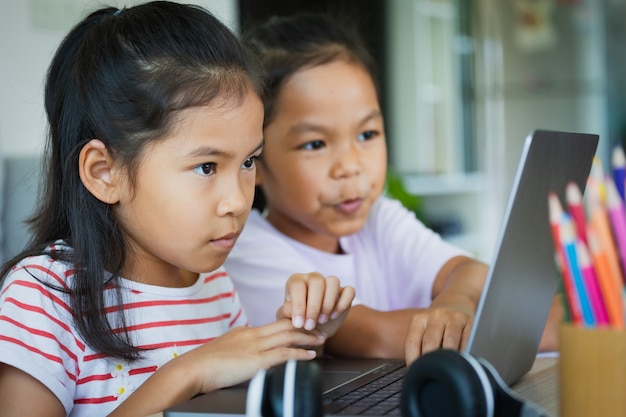 Dos alumnas asiáticas estudian en línea con el maestro por videollamada juntos. Los hermanos reciben educación en el hogar con una computadora portátil durante la cuarentena debido a la pandemia de Covid 19.