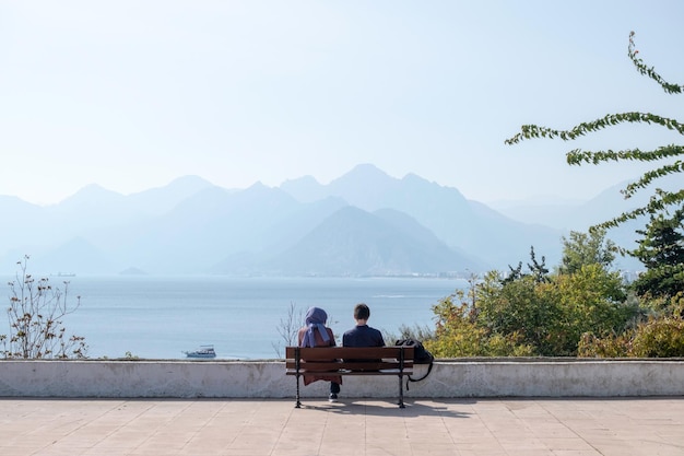 Dos amantes están sentados en un banco frente al mar y las montañas.