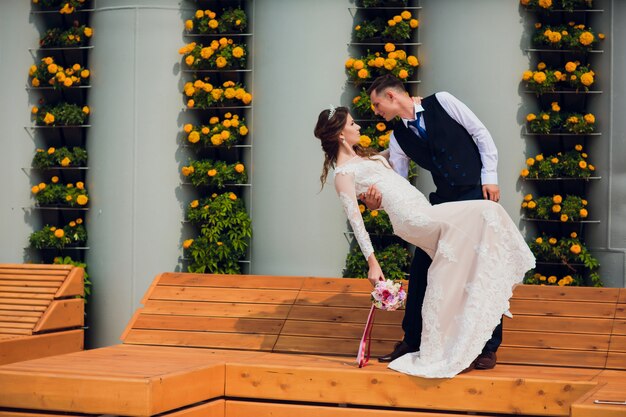 Dos amantes se sientan en un banco, los recién casados se agacharon para descansar en los brazos del otro durante una sesión de fotos de boda, la novia con un vestido blanco y el novio con un hermoso traje retirado en el parque.