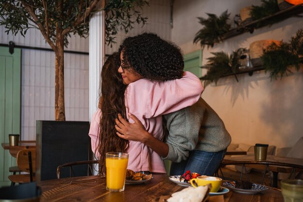 Dos amigas abrazándose después de mucho tiempo sin verse. Están en una cafetería para almorzar.