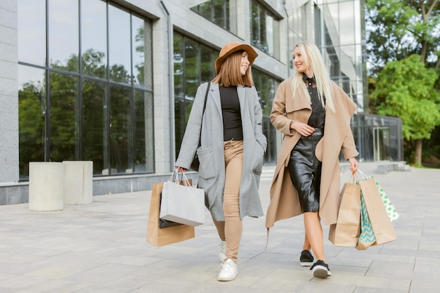 Dos amigas adictas a las compras con ropa de otoño sostienen muchas bolsas de compras y caminan por la ciudad. Estilo de vida, concepto de ocio