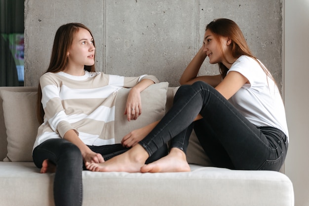 Dos amigas adolescentes alegres hablando mientras está sentado en casa en un sofá