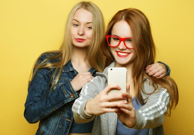 Dos amigas adolescentes en traje de hipster hacen selfie en un teléfono