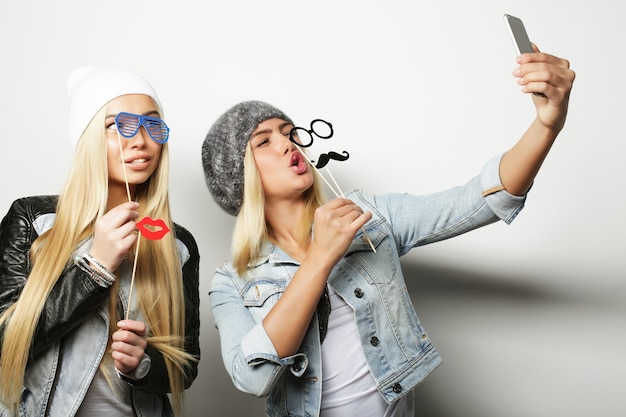 Dos amigas adolescentes vestidas de hipster hacen selfie en un teléfono.