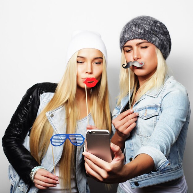 Dos amigas adolescentes vestidas de hipster hacen selfie en un teléfono.