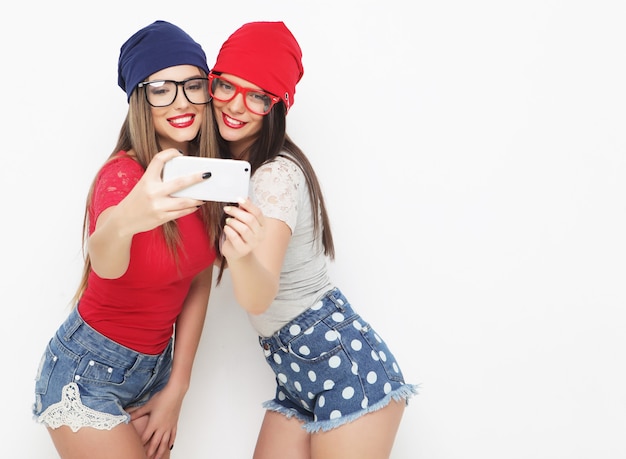 Dos amigas adolescentes vestidas de hipster hacen selfie en un teléfono.