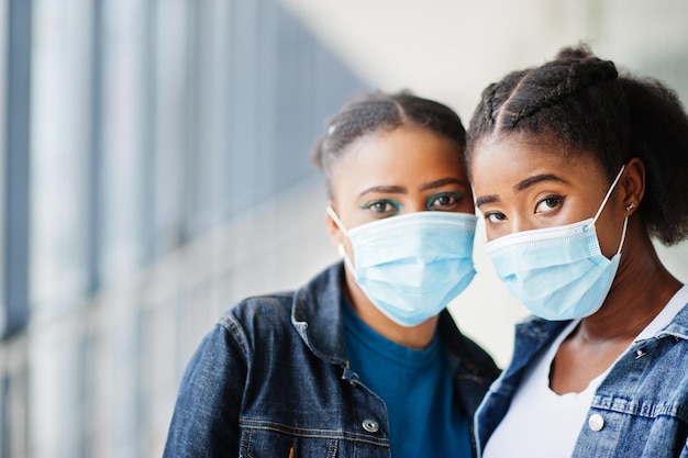 Dos amigas africanas en chaqueta de jeans con máscaras protectoras. Salud concepto de virus, médico.