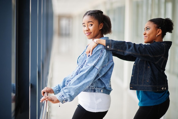 Dos amigas africanas en chaqueta de jeans plantean juntos en el interior.