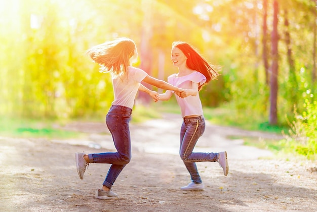 Dos amigas alegres giran cogidas de la mano en un paseo por el bosque de verano