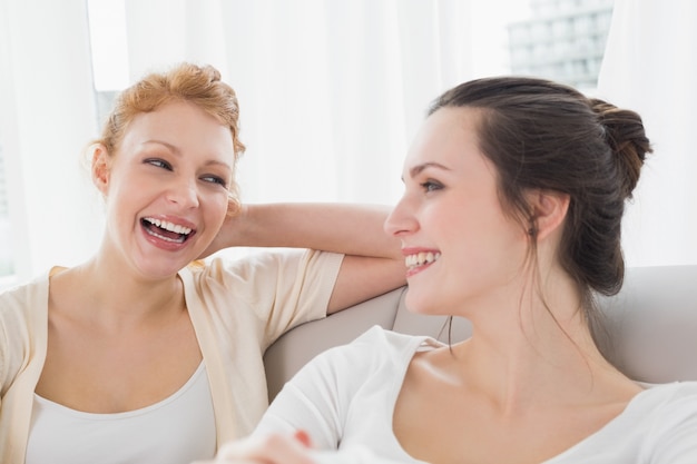 Dos amigas alegres que se sientan en el sofá en la sala de estar