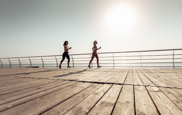 Dos amigas atléticas corriendo a lo largo del terraplén por la mañana temprano