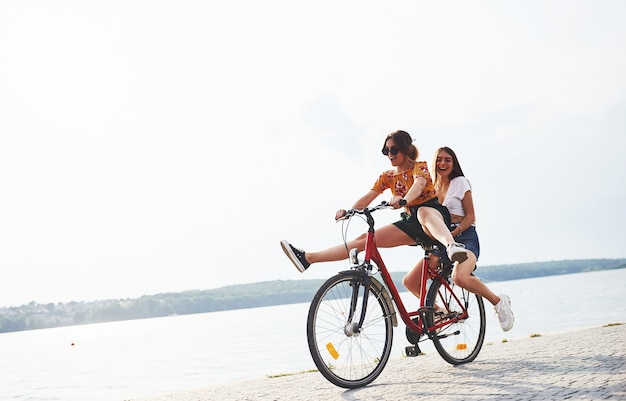 Dos amigas en bicicleta se divierten en la playa cerca del lago.