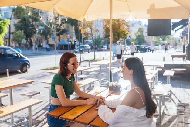 Dos amigas bonitas hablando mientras están sentadas en un bar al aire libre