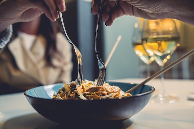 Dos amigas comen fideos junto con un tenedor. Detalle en el plato y en las manos. Foto