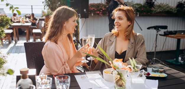 Dos amigas comiendo ostras frescas y bebiendo vino prosecco frío en el atardecer de verano en el restaurante Delicias de mariscos