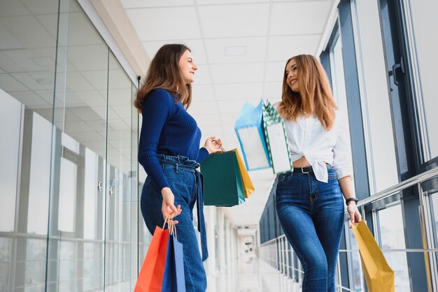 Dos amigas en compras a pie de centro comercial con bolsas