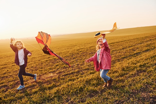 Dos amigas se divierten juntas con un cometa y un avión de juguete en el campo durante el día soleado