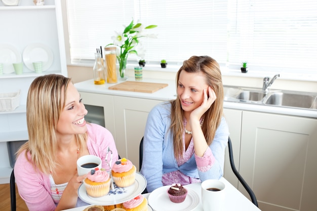 Dos amigas encantadas comiendo pasteles y tomando café en la cocina