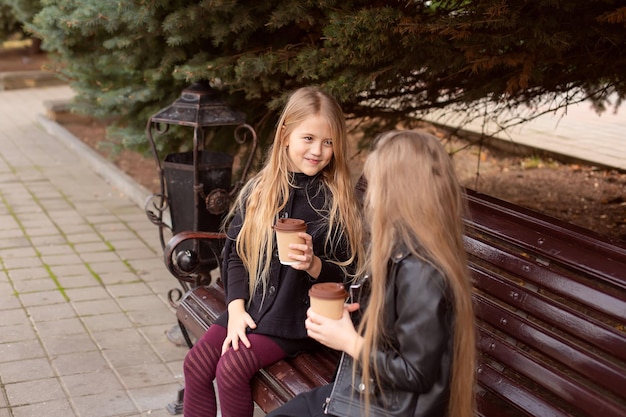 dos amigas están sentadas en un banco del parque con cacao en las manos, charlando dulcemente