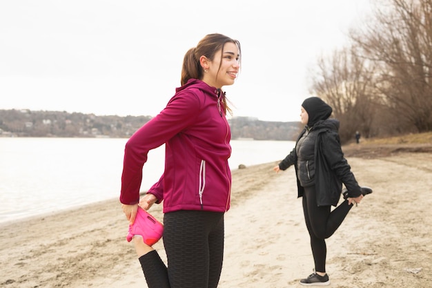 Dos amigas estirando las piernas antes de correr por la mañana