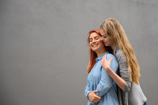 Dos amigas felices se abrazan en el fondo de una pared gris Abrazos suaves de una pareja de lesbianas femeninas LGBT Matrimonio del mismo sexo