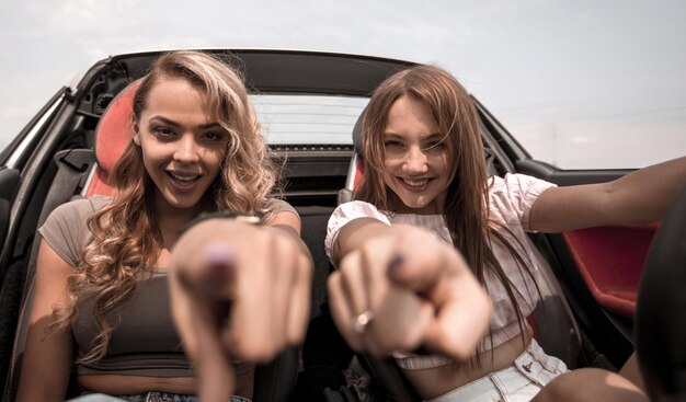 Dos amigas felices sentadas en un auto y señalándote el concepto de elección