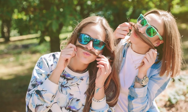 Dos amigas con gafas de sol divirtiéndose haciendo bigotes con su pelo largo. Concepto de tiempo libre y relax.