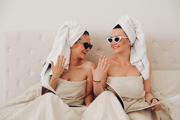 Dos amigas glamurosas felices usando una toalla relajándose juntas