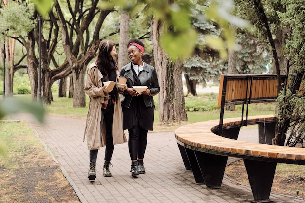 Dos amigas interculturales amorosas con bocadillos caminando en el parque