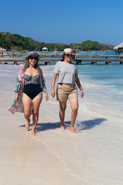 Dos amigas latinas caminando juntas en la playa durante el verano