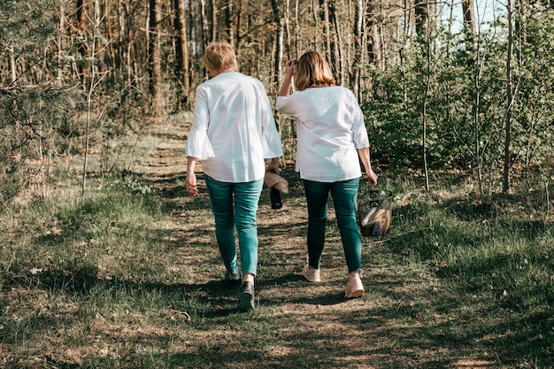 Dos amigas maduras están caminando por el bosque, vista trasera. Estilo de vida activo, pasatiempo