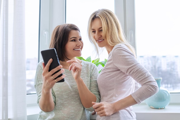 Dos amigas de mediana edad mirando juntas la pantalla del teléfono inteligente