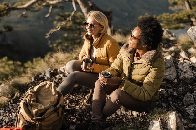 Dos amigas en la naturaleza disfrutando de un descanso para tomar café durante una caminata en las montañas.