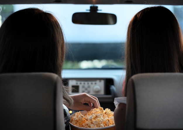 Dos amigas con palomitas de maíz sentadas en el auto mientras ven una película en el cine Enfoque selectivo Entretenimiento actividades de ocio concepto de hobby