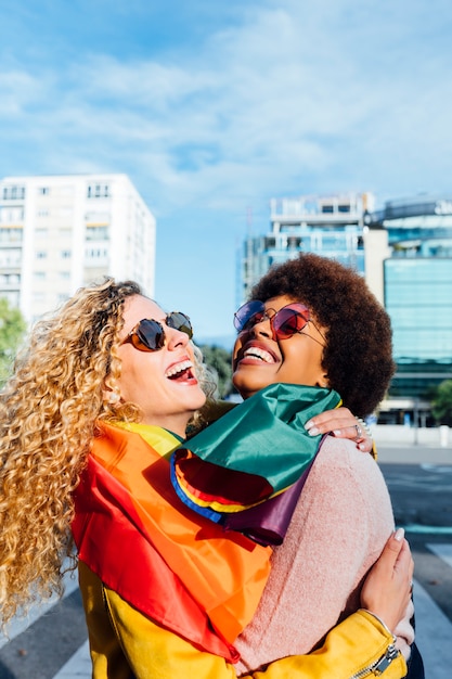 Foto dos amigas pasando el rato en la ciudad saludando a lgbt con la bandera del orgullo