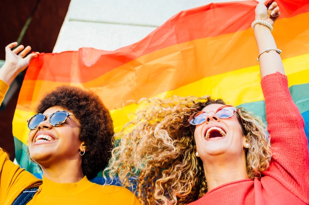 Dos amigas pasando el rato en la ciudad saludando a LGBT con la bandera del orgullo